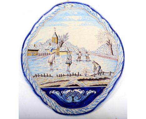 A Dutch Delft Wall Plaque, 19th century, of shaped oval form, painted in colours with figures playing on a frozen lake within