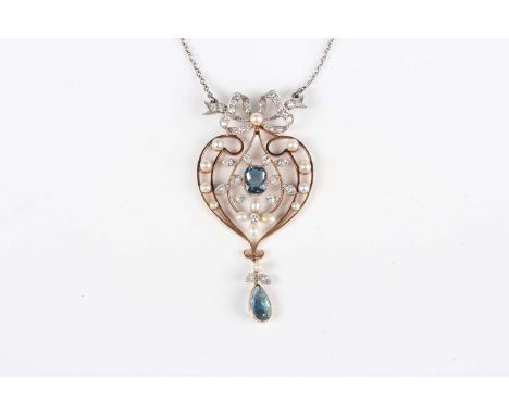 A gold, platinum, sapphire, diamond and seed pearl pendant in scrolling design with ribbon bow surmount, length 5cm, on a sil