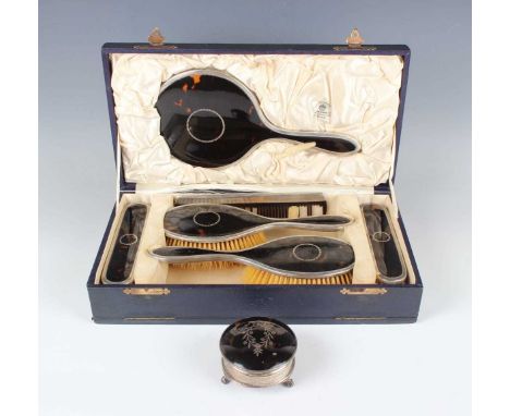 A George V silver and tortoiseshell matched six-piece dressing table set, piqué inlaid with a foliate wreath, comprising hand