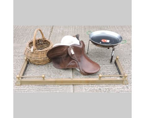A wicker basket, together with a brass fender, a leather saddle and an outdoor paella cooker 
