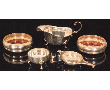 A 1950s hallmarked silver tea strainer and stand, a silver sauce boat with cut edge border and a pair of silver coasters with