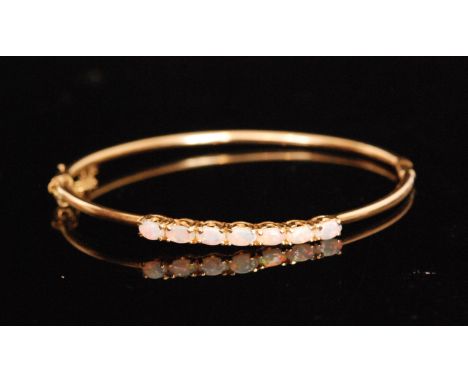 A 14ct opal hinged bangle designed with seven uniform oval opals, claw set to plain cylindrical hinged hoop, weight 6.4g, sta