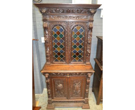 A late 19th to early 20th Century oak bookcase, with arched coloured leaded light glazed doors above a cupboard base detailed