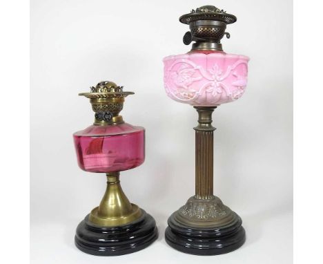 A brass oil lamp, with a cranberry glass font, 33cm high, together with another larger (2)