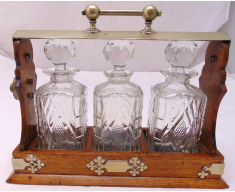 An oak Tantalus with three cut glass decanters with drop stoppers, 29.5 x 38cm