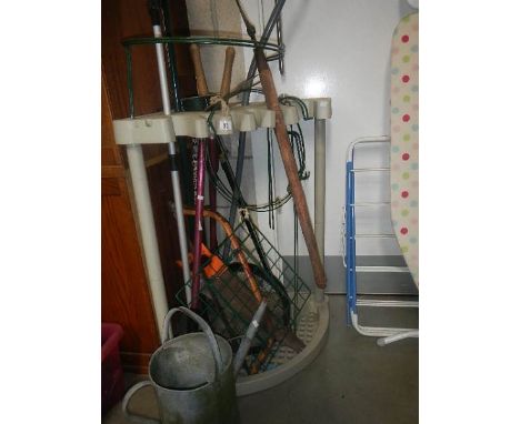 A garden tool rack with tools and a galvanised watering can.