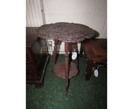 A heavily carved Asian tripod table with lower shelf. The top has a carved goddess holding snakes within a circle and flanked