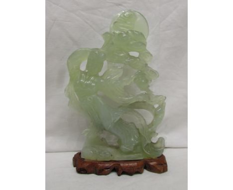 A Chinese style jade type carving depicting female deity in flowing robes supporting clouds and moon, on a low carved wooden 
