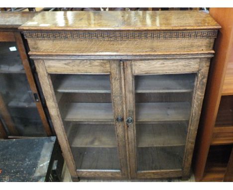 A light oak two door floor standing glazed bookcase with carved top rail