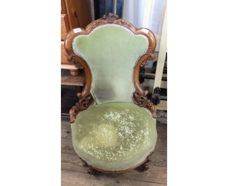 A Victorian walnut nursing chair with elaborate foliate carved sides, fleur de lis motif and light green velvet upholstery