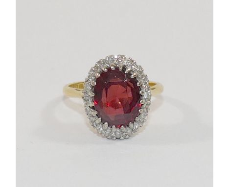 An 18 carat gold oval garnet and diamond cluster ring, London 1989, the oval mixed cut garnet  within 20 small diamond surrou