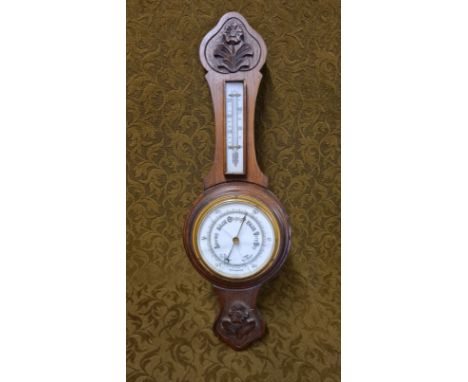 An oak cased aneroid barometer with carved floral decoration (broken glass).