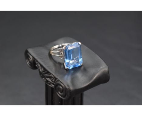 An oversized baguette cut blue topaz ring in a four claw basket mount on an 18ct white gold loop, size M &amp; approx 7.9g
Co