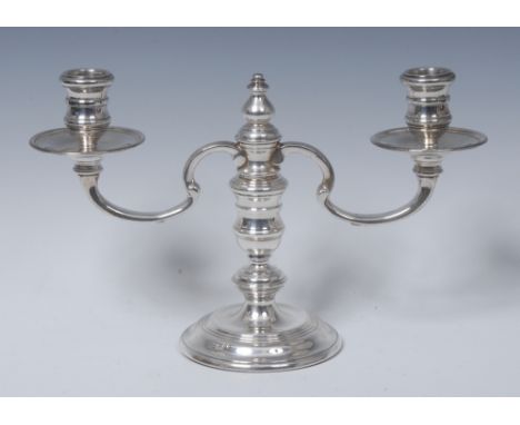 A George I style silver two-light candelabrum, reel shaped sconces, dished drip pans,  knopped pillar, moulded circular base,