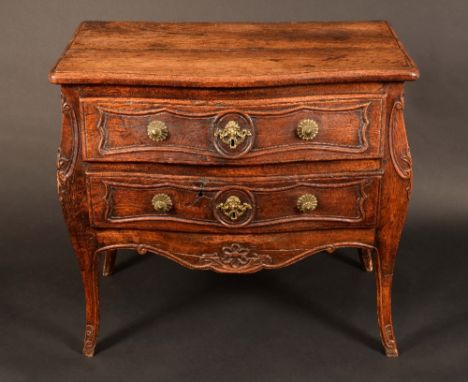 A French provincial oak serpentine commode, moulded oversailing top above two long drawers carved with cartouche shaped reser