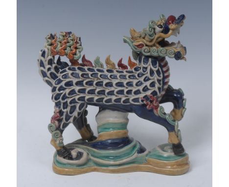 A Chinese stoneware dragon, standing, his scales in relief, coloured in tones of yellow, green, blue and red, shaped base, 18