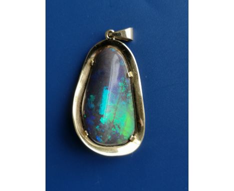 A black opal pendant of polished free-form, claw set within a gold mount, testing as 18ct,  the opal 29mm in length.