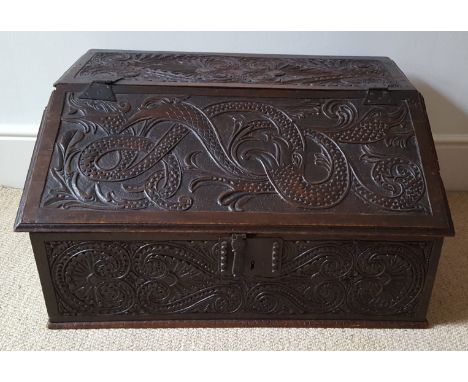 An antique carved oak table top slope front desk, decorated with mythical beasts and birds with serpents' bodies, iron lock a