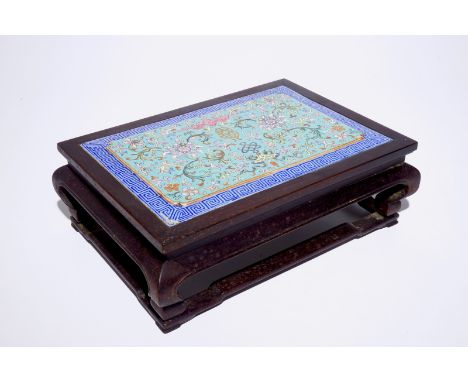 A Chinese famille rose enamel tile plaque mounted in a wood stand, 19th C.  Dim.: 35 x 25 cm - H.: 12 cm (the entire piece)  