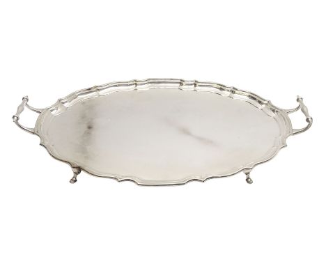 Large early 20th century silver serving tray, of oval form with Chippendale type rim and twin handles, raised upon four hoof 
