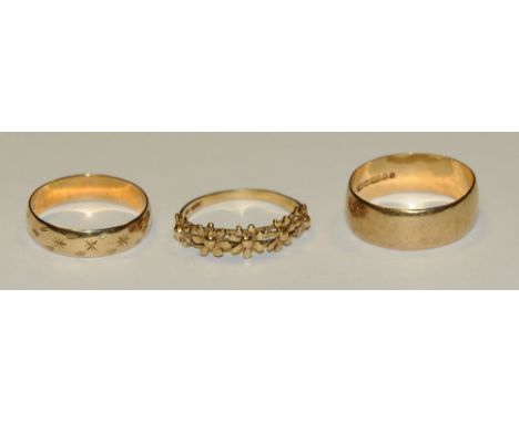 A 9ct gold wedding band, size R; another decorated with stars, size P; an 9ct gold ring in the form of five daisies, size N1/