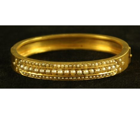 A seed pearl hinge bangle, inset with three lines of creamy white half seed pearls, trefoil terminal accents, unmarked yellow