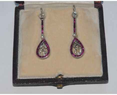 A pair of ruby and diamond drop earrings, each with a floral pear drop and round cut three stone diamond drop within a collar