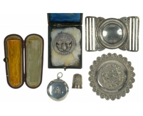 A PIERCED AND ENGRAVED SILVER WAIST CLASP, SHEFFIELD 1910, AN AMBER CIGARETTE HOLDER, CASED, A SILVER BADGE, THIMBLE, COMPACT