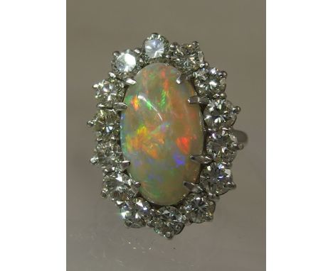 An 18ct white gold opal and diamond cluster ring the high oval opal cabouchon has good flashes of red, green and blue claw se