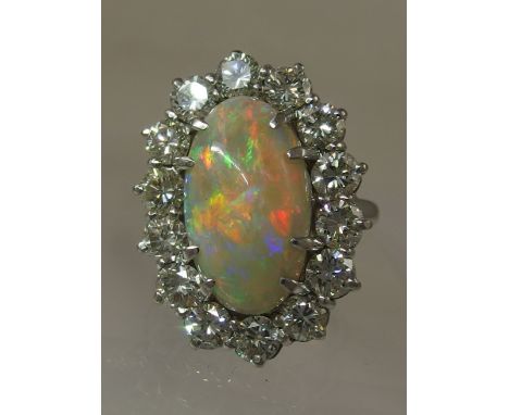 An 18ct white gold opal and diamond cluster ring the high oval opal cabouchon has good flashes of red, green and blue claw se