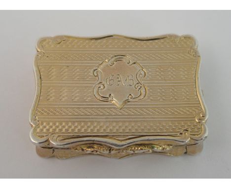 A silver gilt vinaigrette by Alfred Taylor, Birmingham 1850, of rectangular shape with serpentine border, engine turned decor
