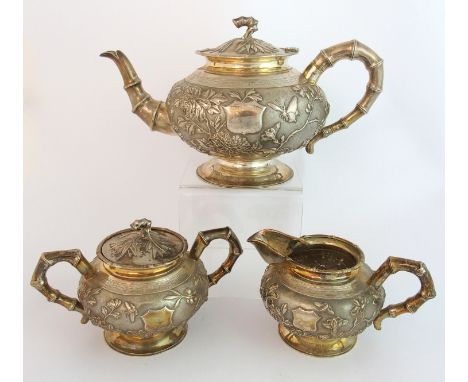 A Chinese silver three piece tea service decorated allover with butterflies amongst chrysanthemum, bamboo and peonies divided