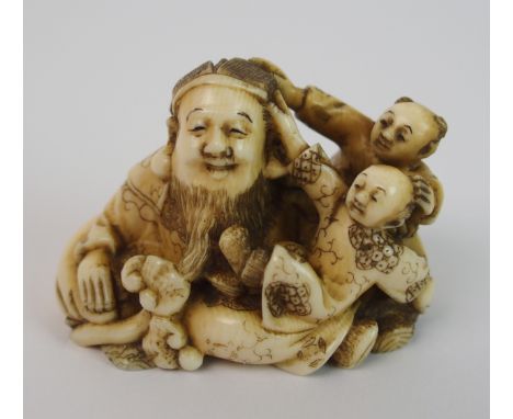 A Japanese ivory netsuke carved with a father and two children playing, he with ruji sceptre, signed on a red lacquered seal,