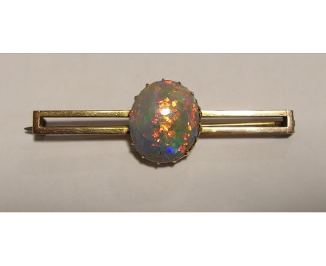 An opal bar brooch  the yellow metal brooch is set with a good black opal rough cabouchon, with every colour of the spectrum 