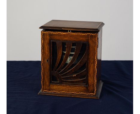 ART DECO OAK SMOKER?S CABINET, the lift up cover above a glazed door overlaid with a ?rising sun? fret cut panel, enclosing a