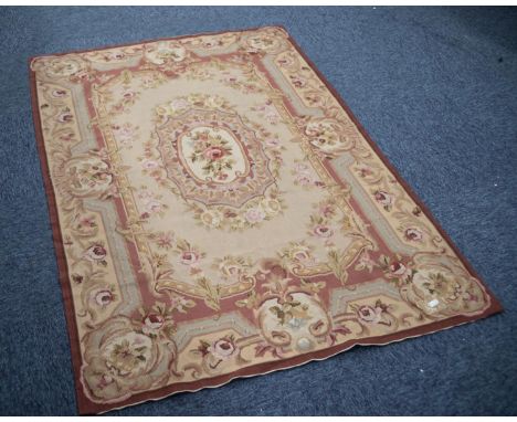 AUBUSSON NEEDLEWORK TAPESTRY RUG with centre oval rose decorated medallion on a fawn field, the elaborate border fawn with ro