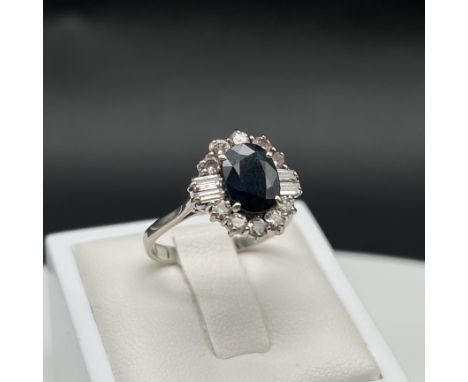 An 18ct white gold deco style sapphire + diamond ring, set with 10mm x 7mm sapphire surrounded by round cut diamonds + baguet