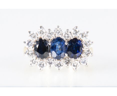 A sapphire and diamond cluster ring, three oval mixed cut sapphires surrounded by eighteen brilliant cut diamonds claw set in