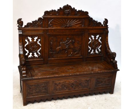 A well carved Victorian oak box seat settle/hall bench, the shaped back decorated with a figure wrestling a lion above the ca
