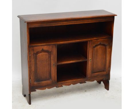 A reproduction oak open bookcase with moulded rectangular top above shelf, small shelf flanked by twin fielded panel cupboard