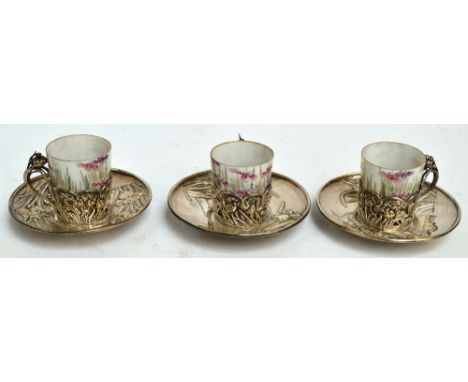 Three Japanese silver cups and saucers embossed with floral motifs, with original ceramic liners hand painted with similar de