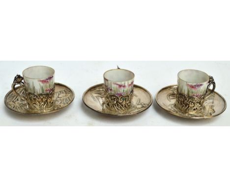 Three Japanese silver cups and saucers embossed with floral motifs, with original ceramic liners hand painted with similar de