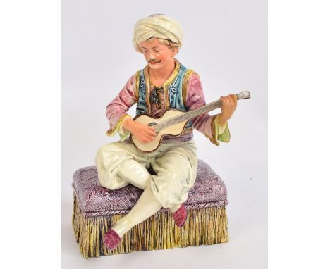 A c.1900 Austrian figure of a man playing a mandolin, wearing Eastern clothes, seated on ottoman with tassels, height 26cm. C