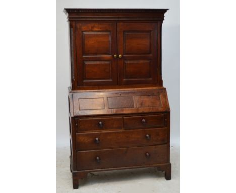 An early 19th century oak bureau bookcase, the dentil moulded cornice above double panelled doors enclosing a shelf above fal