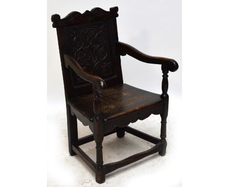 An 18th century oak Wainscot chair with shaped top rail, floral carved panelled back, outswept arms, plank seat, and ring tur