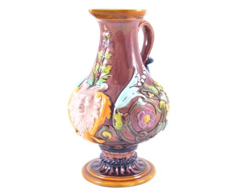 An English majolica face jug, modelled in relief with the mask of a satyr and scrolling floral design, brown ground with yell