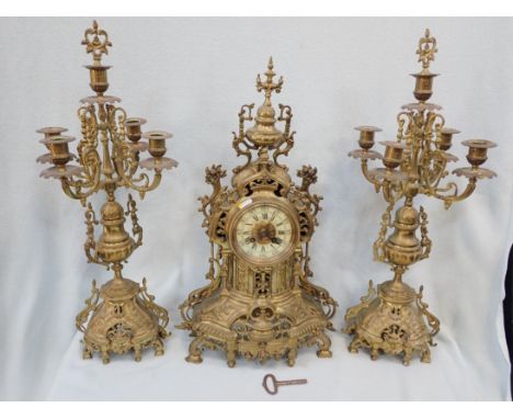 A CAST BRASS CLOCK GARNITURE the clock striking on a bell, flanked by candelabra (one branch detached)