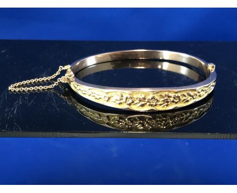 A 9ct hollow rose gold hinged bangle decorated with a floral swag, with safety chain, 7grs approx