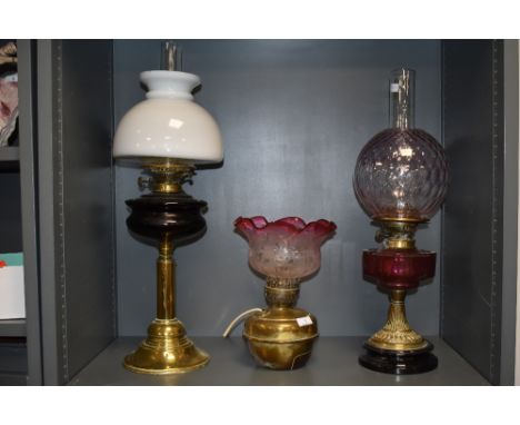Two large antique oil lamps having decorative red glass detailing, also another which has been converted to an electric lamp,