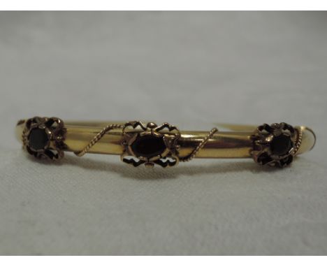 A yellow metal hinged bangle stamped 14K of tubular form having garnet and yellow wire decoration